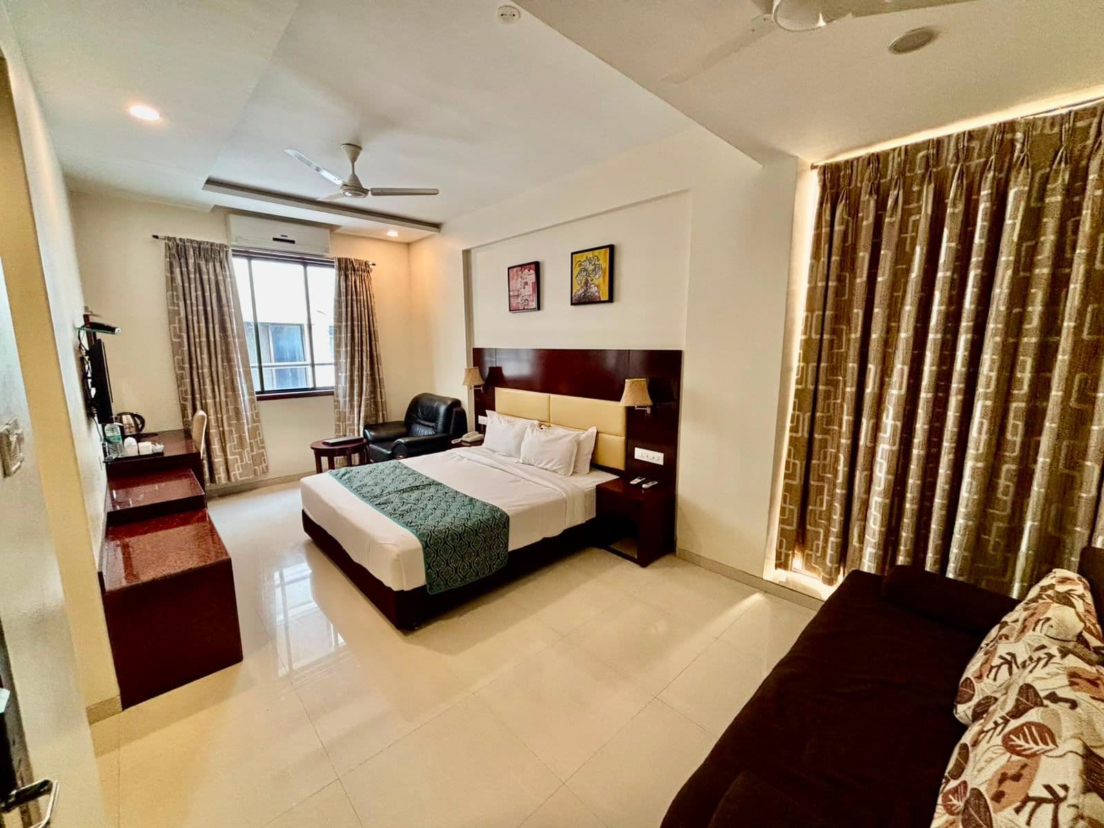 Superior Deluxe room with a king bed, curtained window and sofa at Hotel Sai Jashan