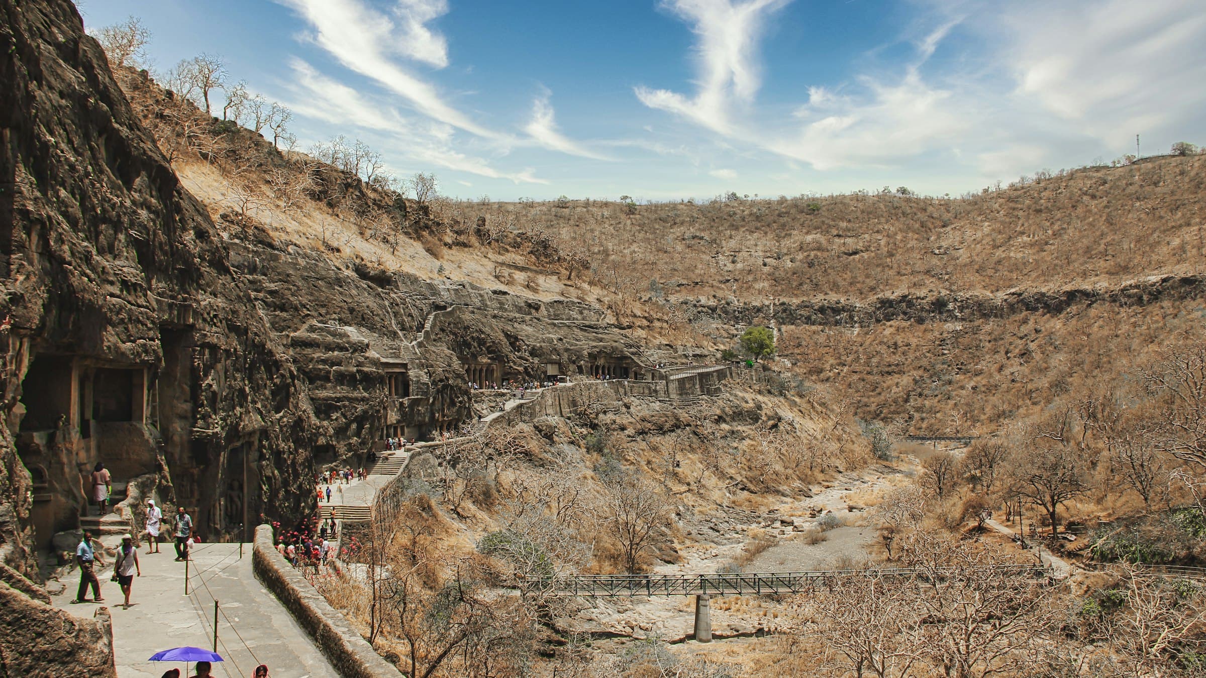 Visitors on the path below the brown hills of the Ajanta Caves gorge in Maharashtra