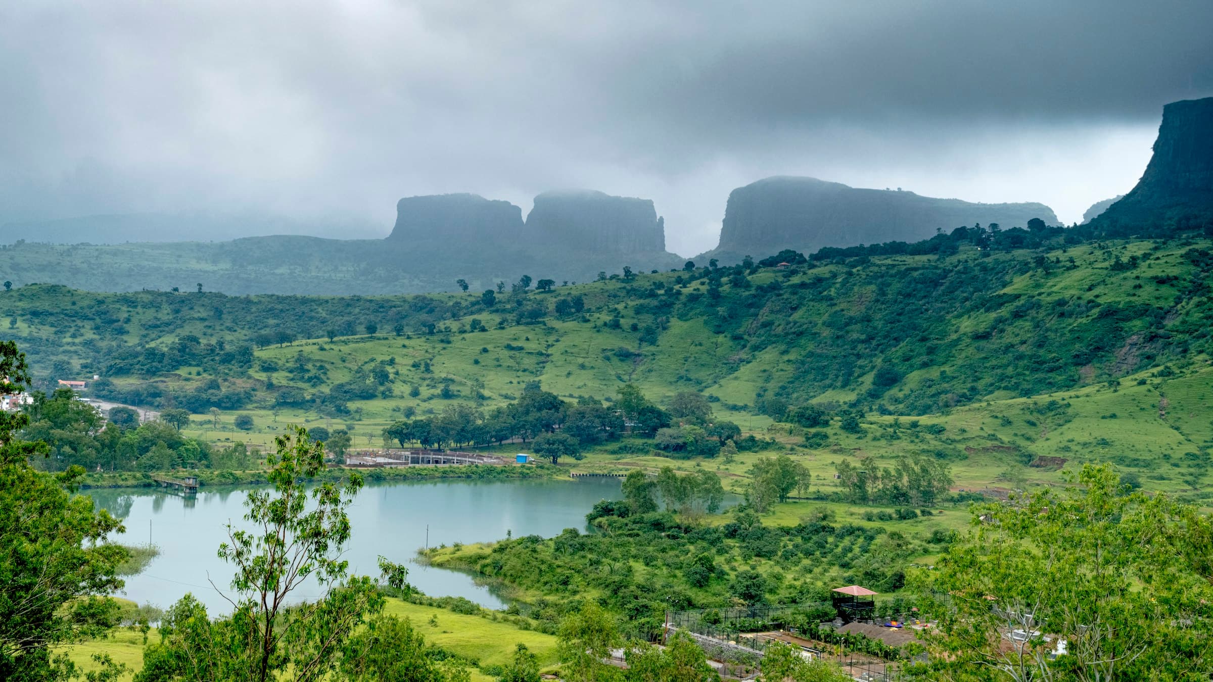 Green Nashik countryside with a lake and mountains in the background