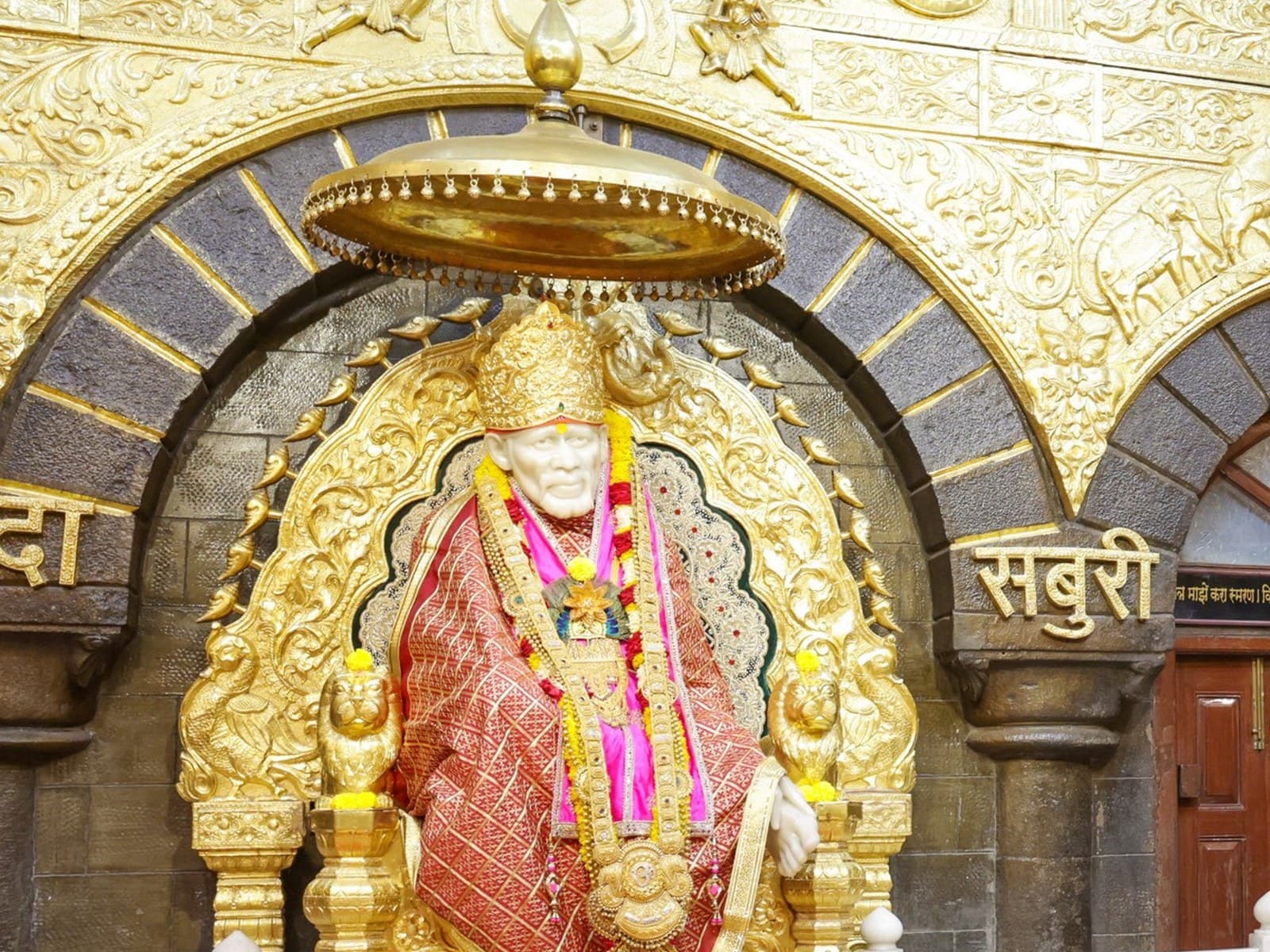 The marble statue of Sai Baba seated on a gilded throne beneath a golden canopy inside the Samadhi Mandir at Shirdi, with an orange cloth draped over the samadhi in front
