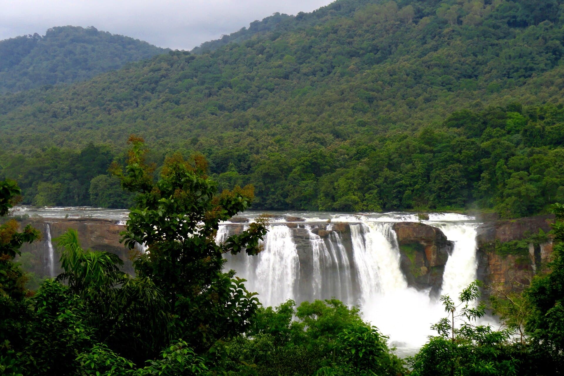 Athirappilly Waterfalls tumbling over a rocky ledge with forested hills behind