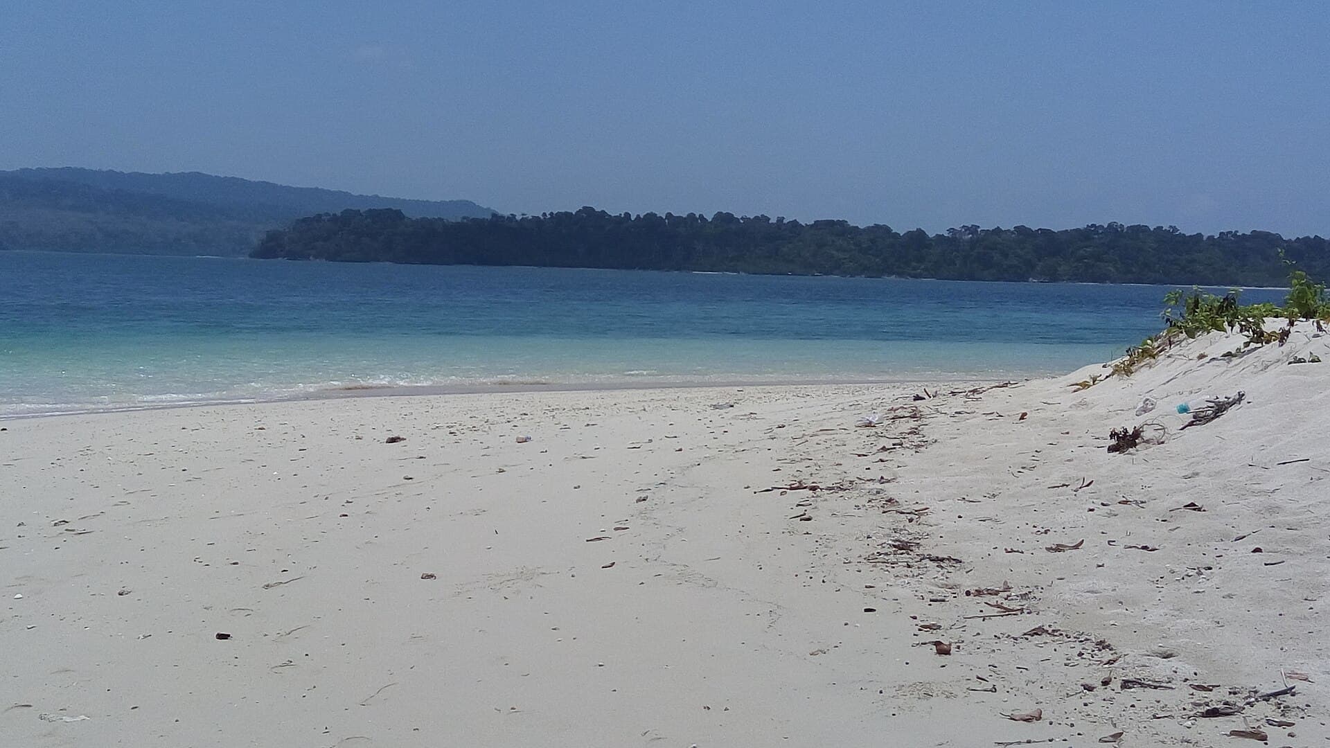 White sand and clear water on Jolly Buoy Island with a forested island across the water